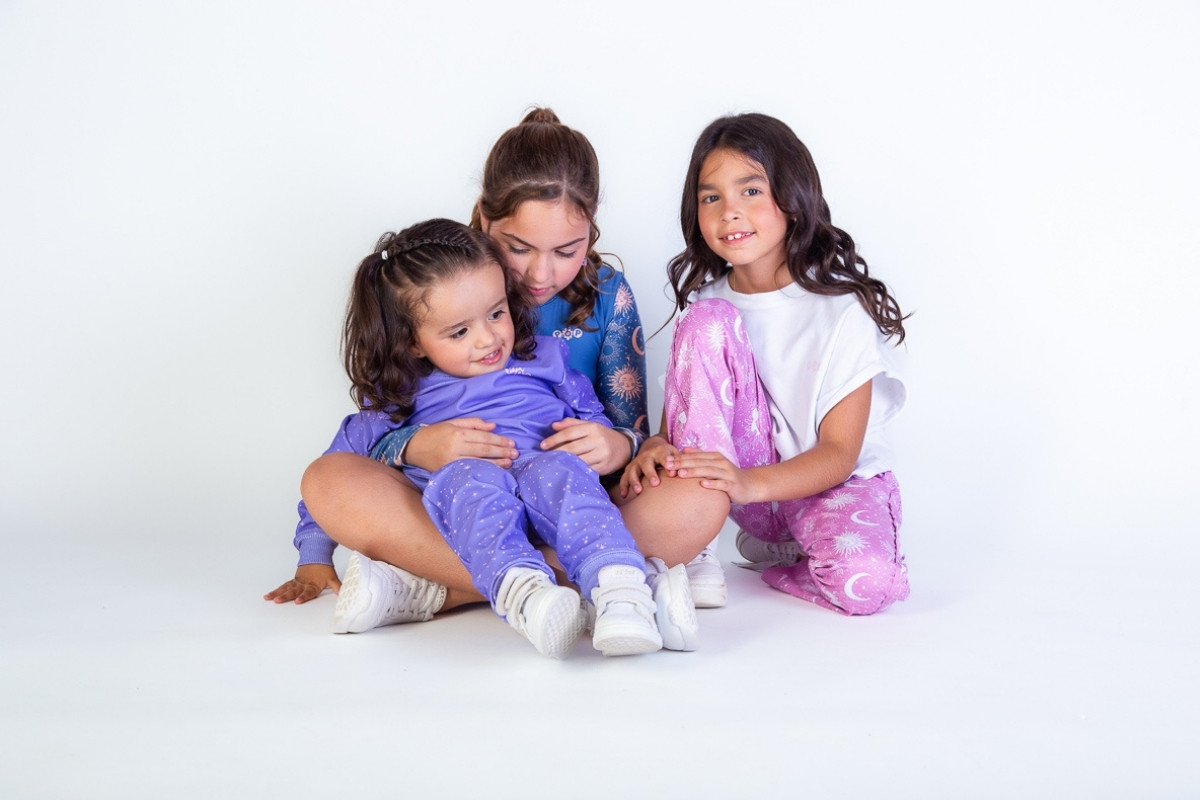 Tres niñas de distintas edades sentadas juntas usando conjuntos de ropa infantil con estampados celestiales; ideal para visualizar el ajuste y la elección de tallas en moda infantil.