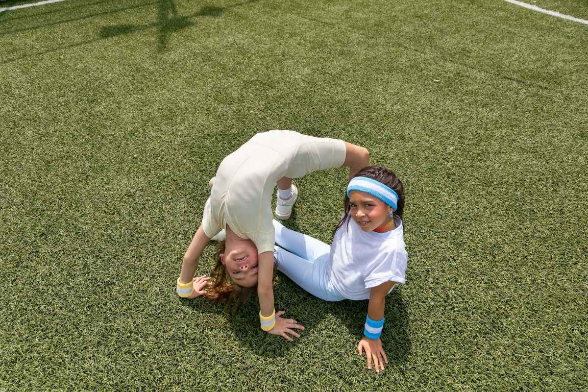Niñas con ropa deportiva flexible y muñequeras realizando ejercicios de gimnasia en un campo de césped.