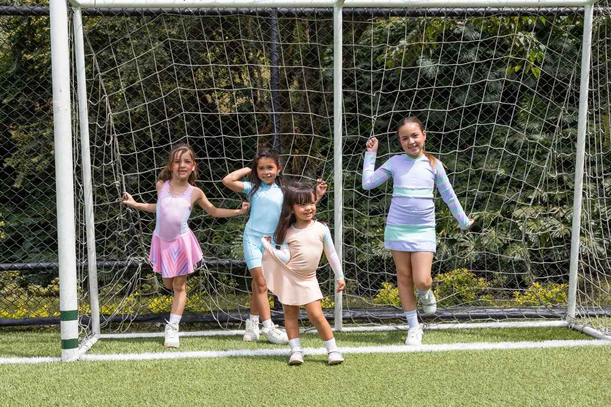 Grupo de niñas de diferentes edades luciendo conjuntos deportivos color pastel frente a una portería de fútbol.