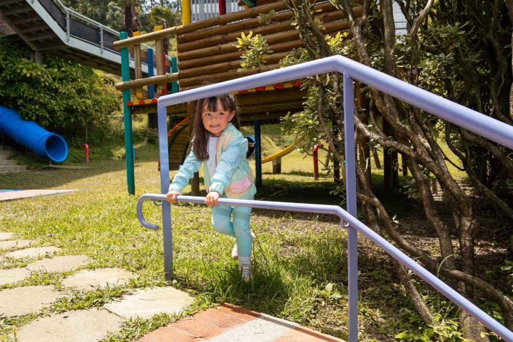 Ropa ideal para el jardín infantil: niña con conjunto deportivo pastel jugando en una zona recreativa al aire libre.