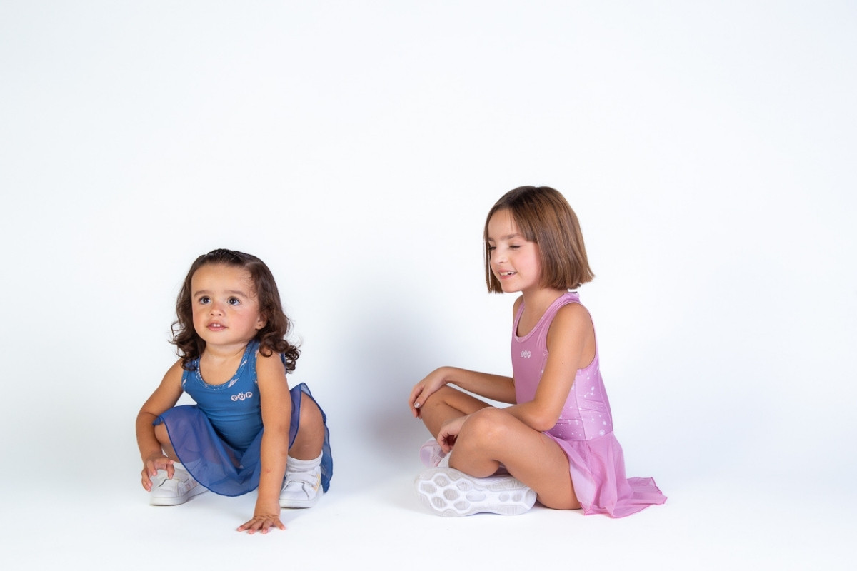 Dos niñas pequeñas sentadas con vestidos deportivos en azul y rosa.