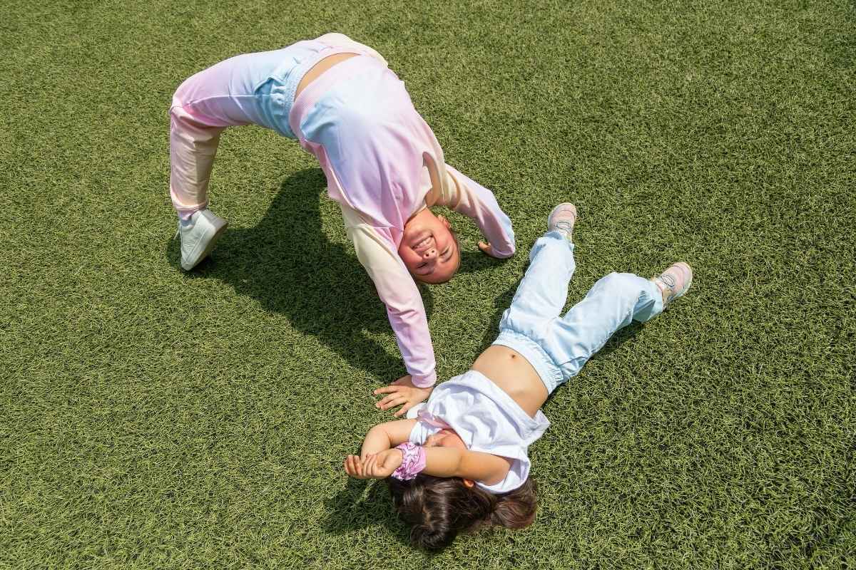 Niñas jugando sobre césped artificial luciendo ropa deportiva infantil en colores pastel, ideal para gimnasia y juego activo.