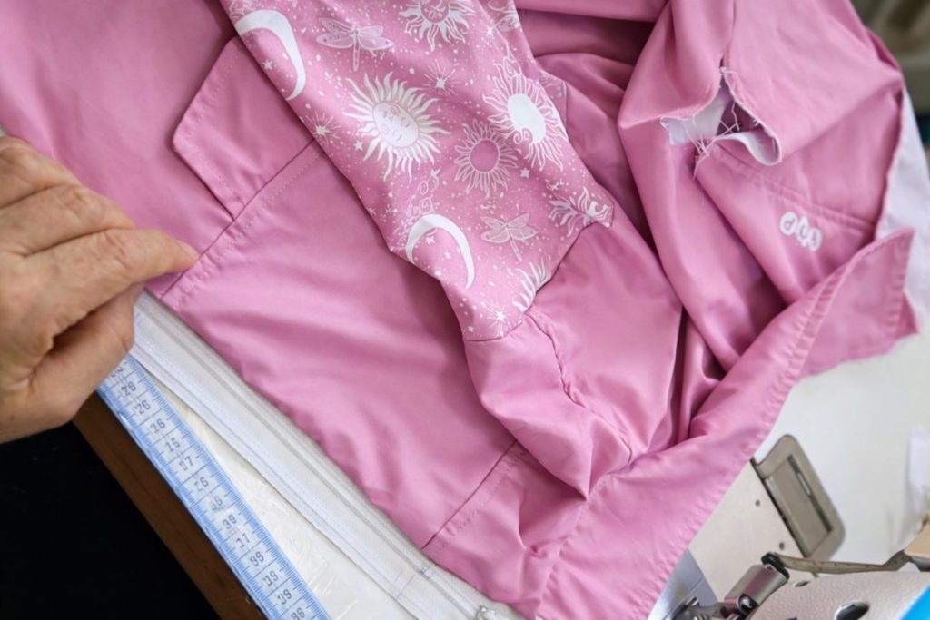 Primer plano de la confección de una chaqueta infantil rosa con textiles suaves y costuras reforzadas.