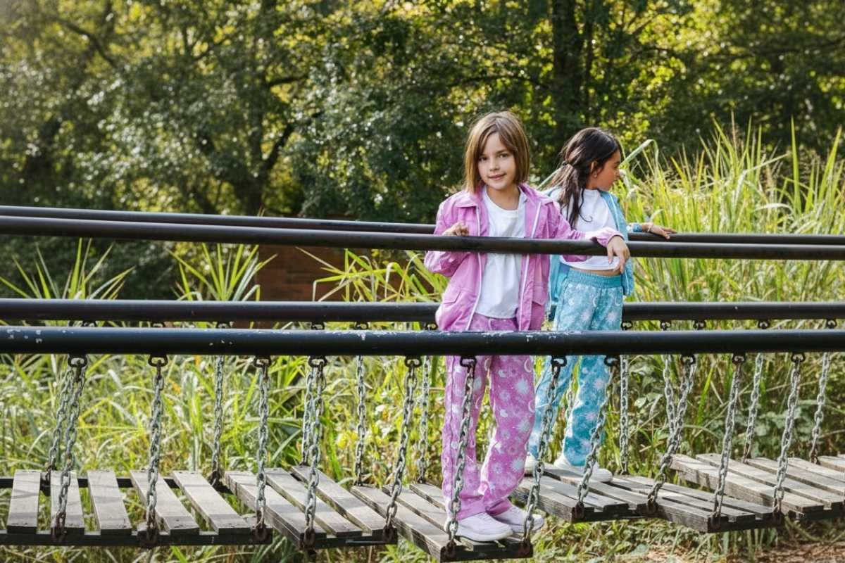 Niñas explorando la naturaleza sobre un puente de madera, vistiendo conjuntos deportivos en rosa y azul con estampados celestiales.